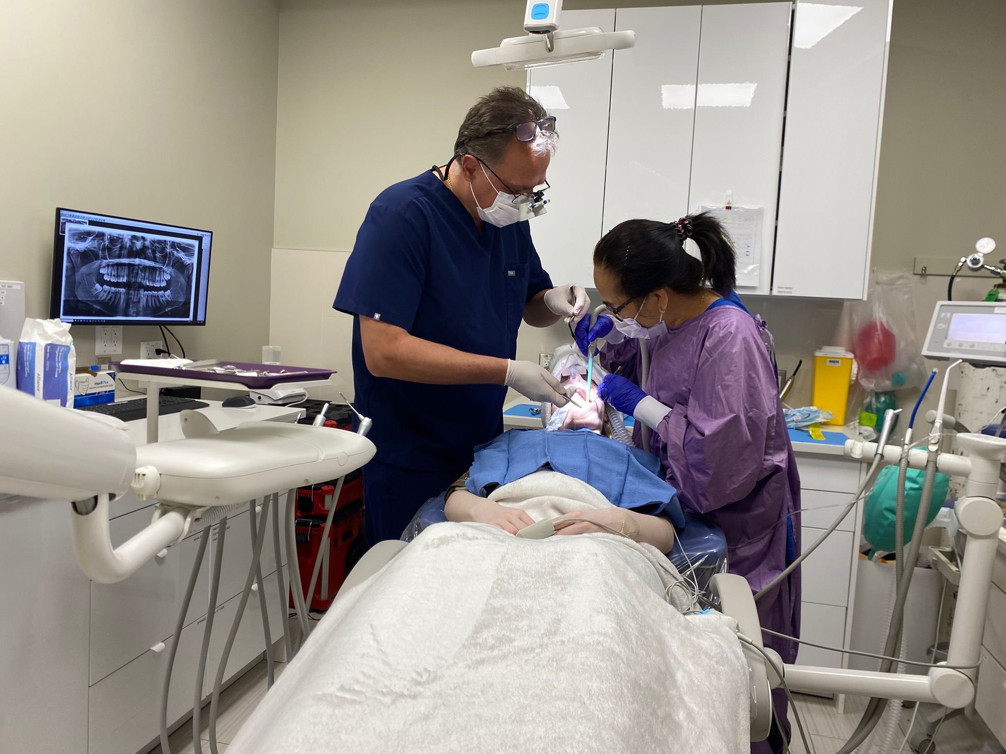 Dr. Koniouchine performing oral surgery with panoramic X-ray on monitor and anesthesia equipment
